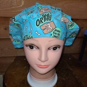 May include: A blue and white patterned surgical scrub hat with the text "Ortho" and "Always Time For A Joint" printed on it. The hat is on a mannequin head.