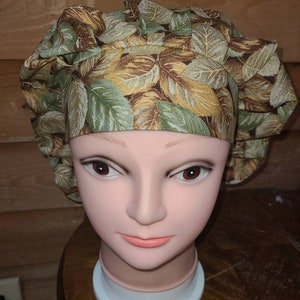 May include: A brown and green patterned scrub hat with a leaf design. The hat is on a mannequin head.