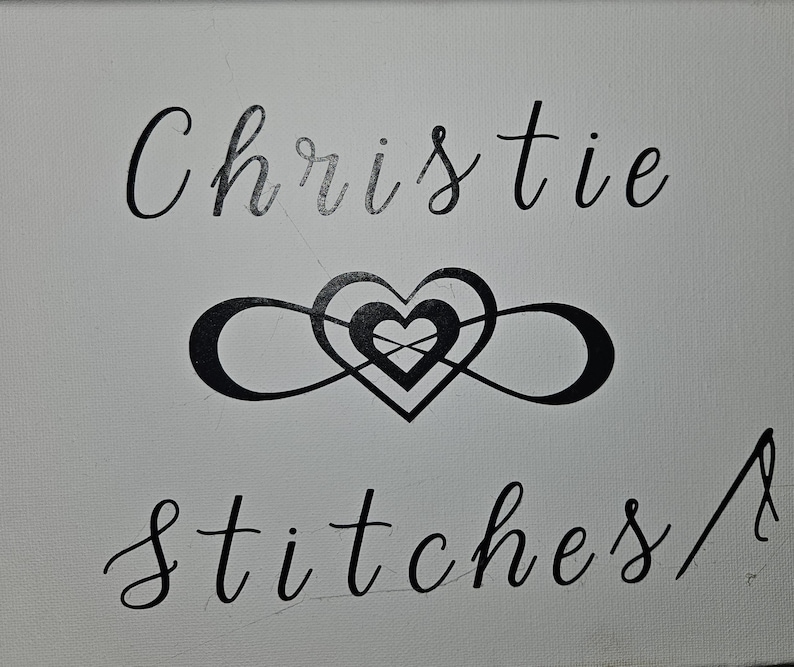 May include: A white canvas with black lettering that reads "Christie Stitches" and a black infinity symbol with a heart inside.