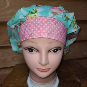May include: A turquoise and pink patterned surgical scrub hat with a pink polka dot band. The hat is made of fabric and has a ruffled edge.