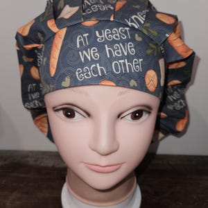 May include: A blue and orange patterned scrub hat with the text "At yeast we have each other".