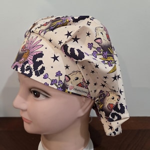 May include: A cream-colored scrub cap featuring a repeating pattern of opossums, purple lavender sprigs, black stars, and leopard print accents. The fabric cap includes a small white tag with the text ChristieStitches and a pink heart icon.