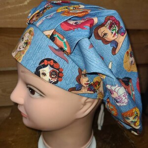 May include: A blue scrub hat with a print of various Disney princesses with Day of the Dead makeup. The hat has a white drawstring.