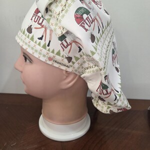 May include: A white scrub cap featuring a repeating Christmas-themed pattern with green pine trees, brown poop emojis, and text that reads "Shitter's Full". The fabric also includes the brand name "ChristieStitcher" with a small red heart icon.
