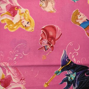 May include: Pink fabric with a repeating pattern of Disney princesses and characters. The characters include Sleeping Beauty, Prince Phillip, Maleficent, and an owl.