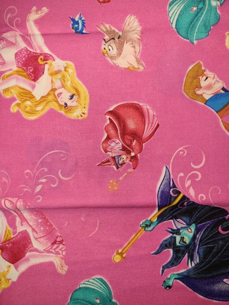 May include: Pink fabric with a repeating pattern of Disney princesses and characters. The characters include Sleeping Beauty, Prince Phillip, Maleficent, and an owl.