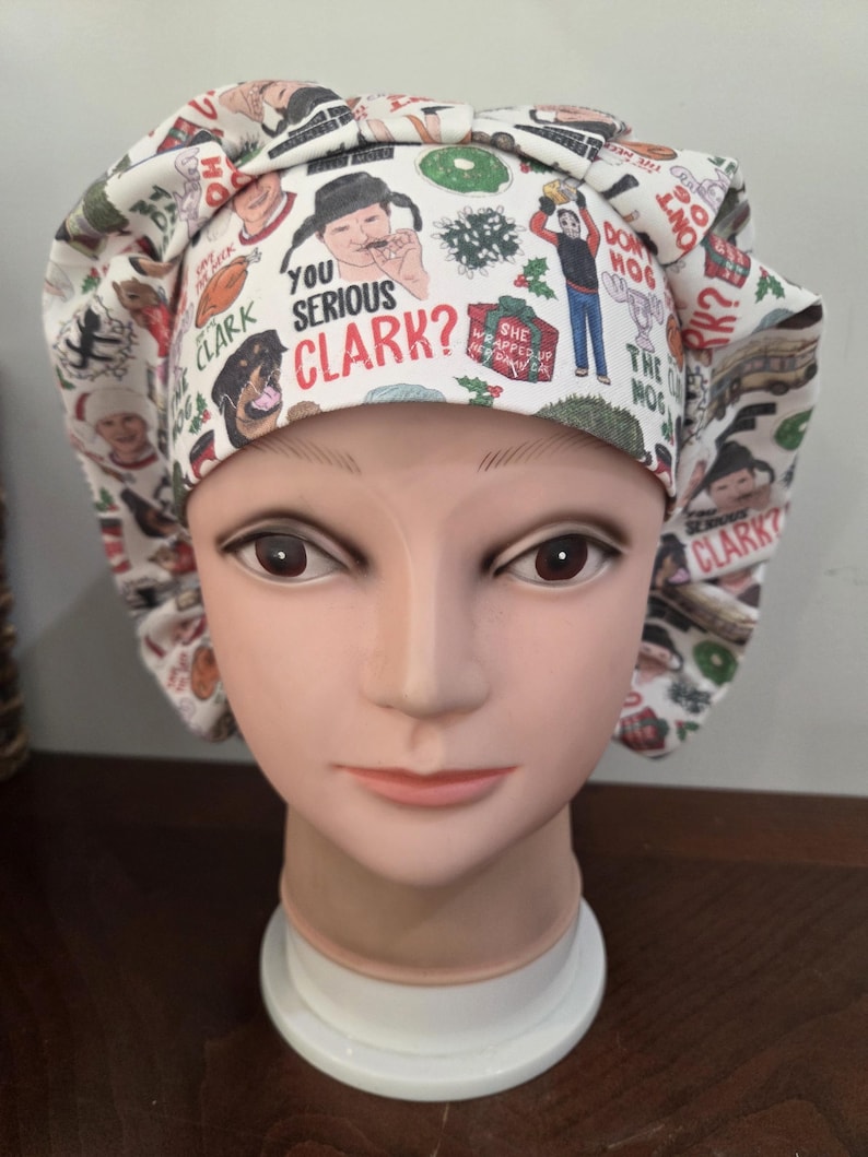 May include: A white scrub cap featuring a repeating pattern of Christmas-themed illustrations and text including the phrase YOU SERIOUS CLARK?, a turkey, a dog, a gift box labeled SHE WRAPPED UP HER DAMN CAT, and various holiday icons.