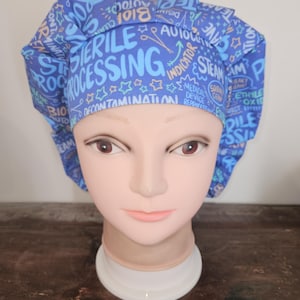 May include: Blue surgical scrub hat with a white and yellow print of medical terms and symbols, including "sterile processing", "decontamination", "steam", and "indicator".