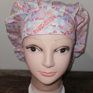 May include: A chef's hat with a light blue background and a pattern of Smarties candy. The hat is made of fabric and has a ruffled design around the edges. The text "Smarties" is visible on the hat.