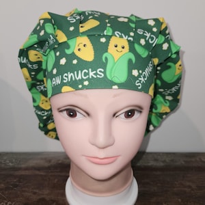 May include: Green scrub hat with a corn on the cob pattern and the text "Aw shucks".