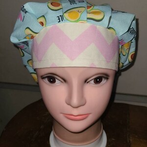 May include: A blue and white scrub hat with a pink and white chevron pattern. The hat has a print of avocados with the text "I love to avocado" on it.