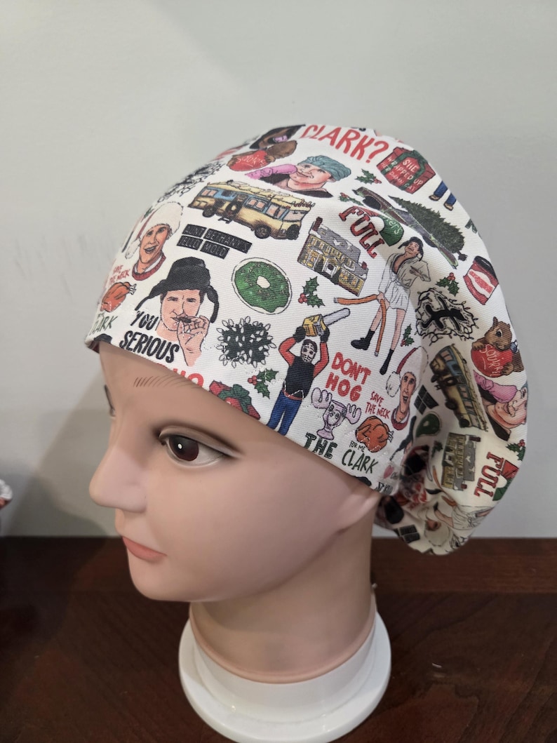 May include: A white scrub cap featuring a colorful all-over print of characters, vehicles, and holiday-themed objects from a Christmas movie. The fabric includes text such as CLARK?, FULL, YOU SERIOUS, DON'T HOG, and SAVE THE NECK.