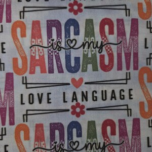 May include: Light blue fabric with the words "LOVE LANGUAGE" and "SARCASM is my" in a repeating pattern. The word "SARCASM" is in orange, purple, blue, and green. The text is decorated with hearts and flowers.