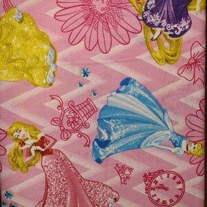 May include: Pink fabric with a repeating pattern of Disney princesses. The princesses are Cinderella, Rapunzel, and Aurora. The fabric also features a clock, a flower, and a birdcage.