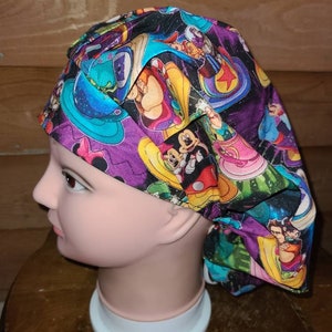 May include: A purple, green, and black scrub hat with a colorful cartoon print featuring Mickey Mouse, Minnie Mouse, and other Disney characters.