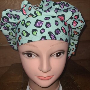 May include: A turquoise blue surgical scrub hat with a leopard print pattern featuring colorful glitter accents.