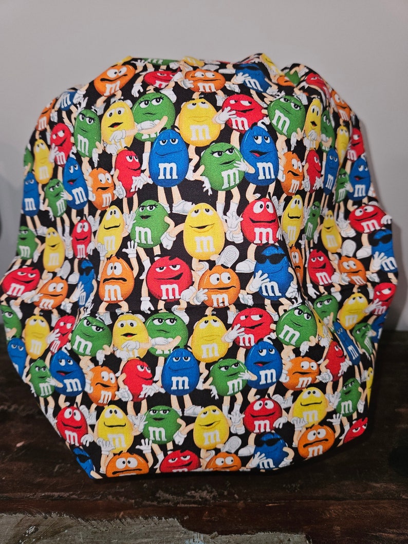 Pu&ograve; includere: Tessuto nero con un motivo ripetuto di personaggi M&M's colorati. I personaggi indossano tutti guanti bianchi e hanno espressioni facciali diverse.