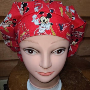 May include: Red scrub hat with a Mickey Mouse baseball theme. The hat features Mickey Mouse in a baseball uniform with the St. Louis Cardinals logo.