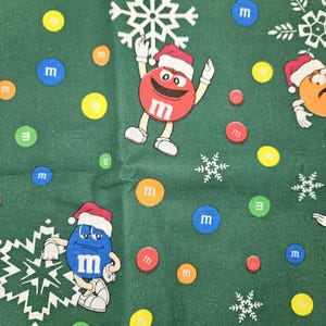 Pu&ograve; includere: Tessuto verde con un motivo ripetuto di M&M's che indossano cappelli da Babbo Natale e tengono fiocchi di neve. Gli M&M's sono rossi, blu, gialli e arancioni. Ci sono anche M&M's sparsi in vari colori.