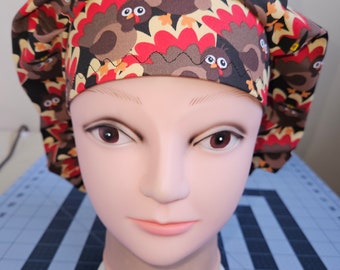 Könnte beinhalten: Eine braune, rote und gelbe gemusterte OP-Mütze mit einem Design von Truthähnen. Die Mütze befindet sich auf einem Mannequin-Kopf.