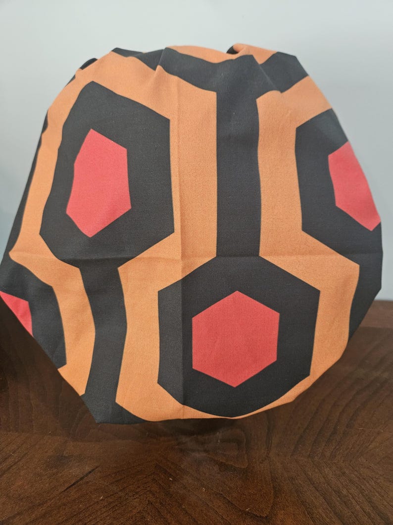May include: A fabric item with a repeating geometric pattern of black, orange, and red hexagons. The item is folded, creating a rounded shape. The design is reminiscent of a classic carpet pattern.