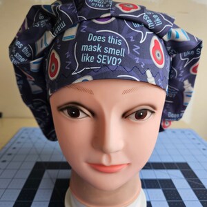 May include: A blue scrub hat with a white and blue pattern. The hat has a white speech bubble with the text "Does this mask smell like SEVO?" printed on it.