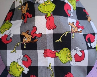 May include: A black and white buffalo plaid fabric with a repeating pattern of the Grinch wearing a Santa hat and a reindeer.