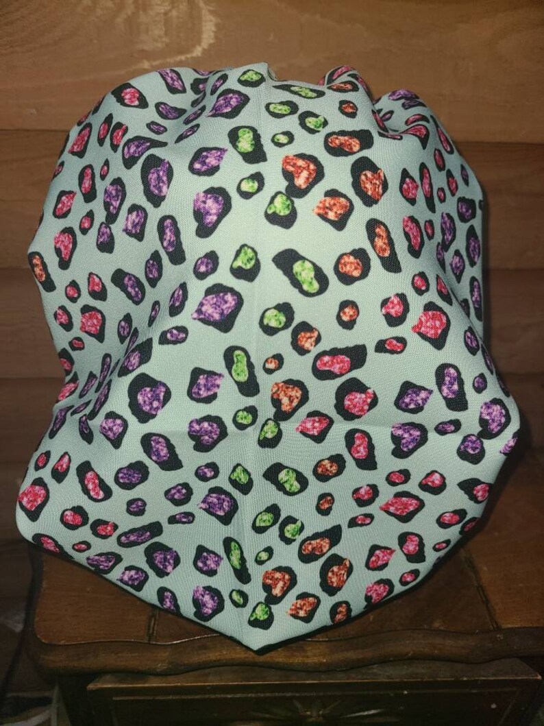 May include: A light blue fabric scrunchie with a colorful leopard print pattern. The print features pink, green, orange, and purple spots on a light blue background.