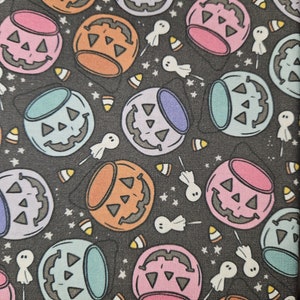 May include: A black fabric with a repeating pattern of colorful jack-o'-lantern buckets. The buckets are filled with candy corn and have a variety of colors including orange, pink, blue, and purple. There are also small white ghosts scattered throughout the pattern.