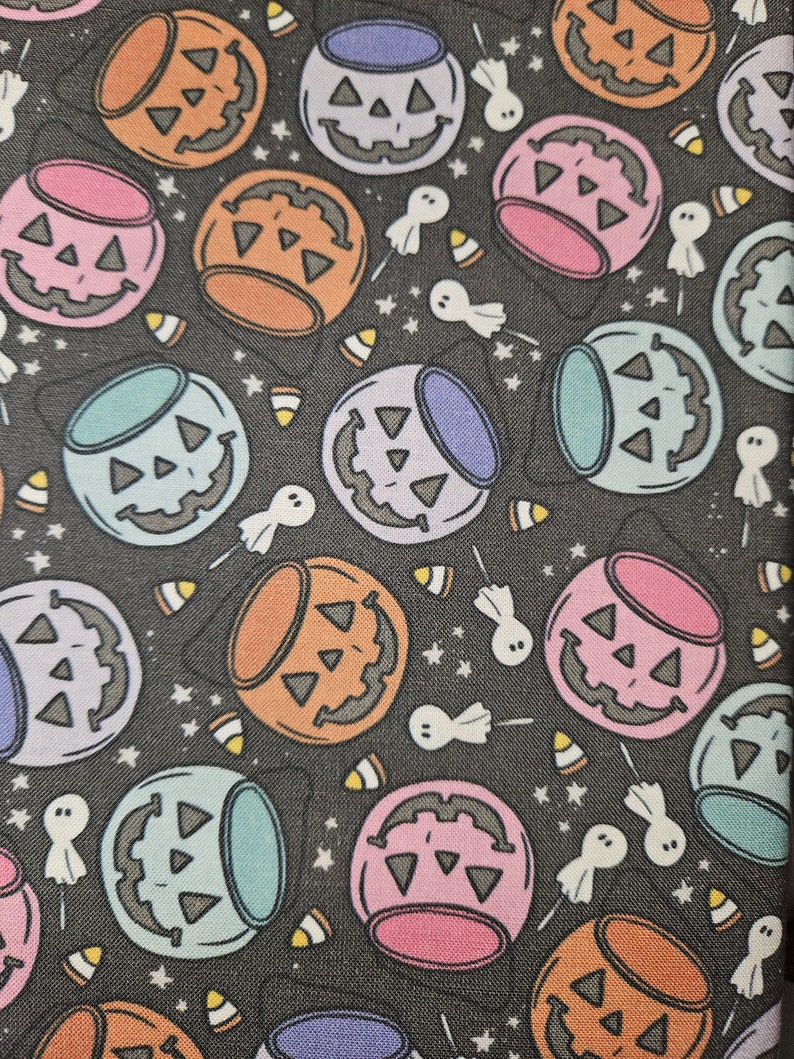 May include: A black fabric with a repeating pattern of colorful jack-o'-lantern buckets. The buckets are filled with candy corn and have a variety of colors including orange, pink, blue, and purple. There are also small white ghosts scattered throughout the pattern.