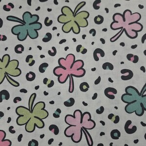 May include: White fabric with a repeating pattern of green, pink, and teal four-leaf clovers and black leopard spots.