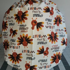 May include: A white fabric with a repeating pattern of turkeys and the text "Gobble 'til you Wobble!" in orange and brown.