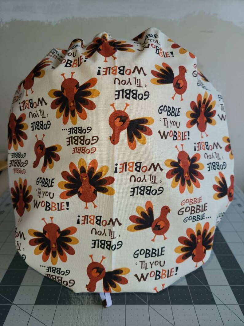 May include: A white fabric with a repeating pattern of turkeys and the text "Gobble 'til you Wobble!" in orange and brown.