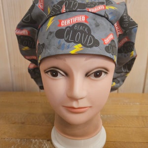 May include: A gray and black scrub hat with a repeating pattern of clouds and lightning bolts. The text "CERTIFIED BLACK CLOUD" is printed on the hat.