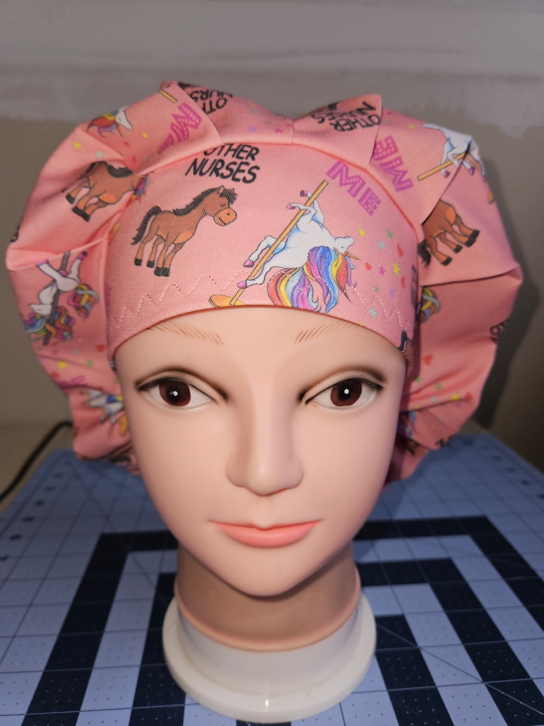 K&ouml;nnte beinhalten: Rosa chirurgische M&uuml;tze mit einem Einhorn-, Pferde- und Sternenmuster. Die M&uuml;tze tr&auml;gt den Text "Other Nurses" und "Me".