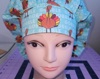 Könnte beinhalten: Eine hellblaue OP-Mütze mit einem Muster aus Truthähnen und dem Wort "gobble", das sich wiederholt. Die Mütze befindet sich auf einem Mannequin-Kopf.