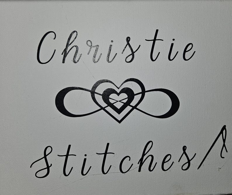 May include: A white canvas with the words "Christie stitches" in black cursive script. A black heart is intertwined with an infinity symbol in the center of the canvas.