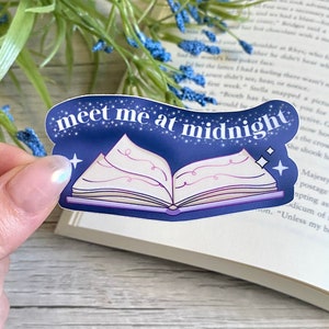 May include: A blue and white sticker with a book and stars. The text on the sticker reads "meet me at midnight".