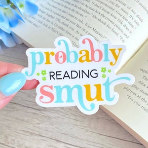 May include: A white sticker with the text "probably reading smut" in colorful letters. The words "probably" and "smut" are in pink, yellow, and blue. The word "reading" is in black.