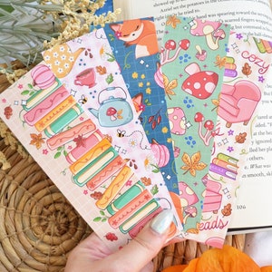 May include: Set of five colorful bookmarks featuring different patterns. One bookmark has a stack of books with autumn leaves, another has a teapot and flowers, another has a fox, another has mushrooms, and the last one has a cozy armchair and the word "cozy".