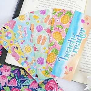 May include: A set of six colorful bookmarks featuring summer-themed designs. The bookmarks have a variety of patterns, including pineapples, flip-flops, seashells, and a flamingo. The text "Sunshine Books" and "Beach Reader" are featured on two of the bookmarks.