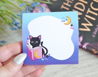 May include: A square sticky note with a blue gradient background and a large white cloud-shaped writing area. It features a black cat reading a pink book with a yellow crescent moon, surrounded by small crystals, flowers, and a moon.