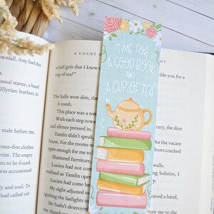 May include: A teal blue bookmark featuring a white teapot and a stack of books. The bookmark has the text "Time for a good book and a cup of tea".