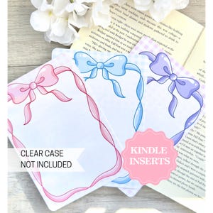May include: Three printable bookmark designs featuring a ribbon and bow border. The designs are pink, blue, and purple. The text "CLEAR CASE NOT INCLUDED" is at the bottom of the pink design. The text "KINDLE INSERTS" is at the bottom of the blue design.