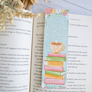 May include: A teal blue bookmark featuring a stack of colourful books and a cup of coffee. The bookmark has the text "Time for a good book and a cup of coffee" and the word "STARLIGHT" in the top right corner.