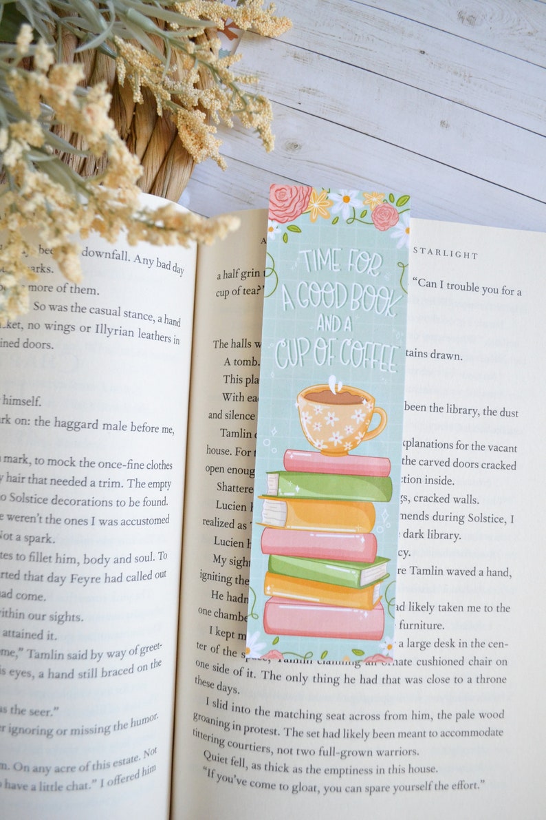 May include: A teal blue bookmark featuring a stack of colourful books and a cup of coffee. The bookmark has the text "Time for a good book and a cup of coffee" and the word "STARLIGHT" in the top right corner.