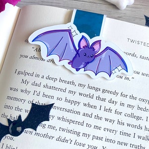 May include: A purple bat with stitched wings and sparkling eyes is on a book page with text that reads "you almost dro ou in." The text is from a book about twisted words and tastes.