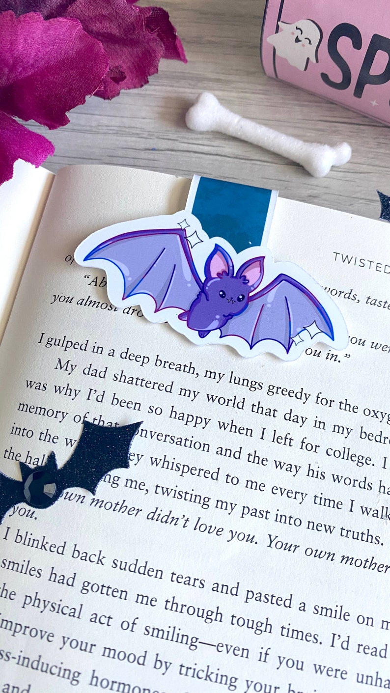 May include: A purple bat with stitched wings and sparkling eyes is on a book page with text that reads "you almost dro ou in." The text is from a book about twisted words and tastes.