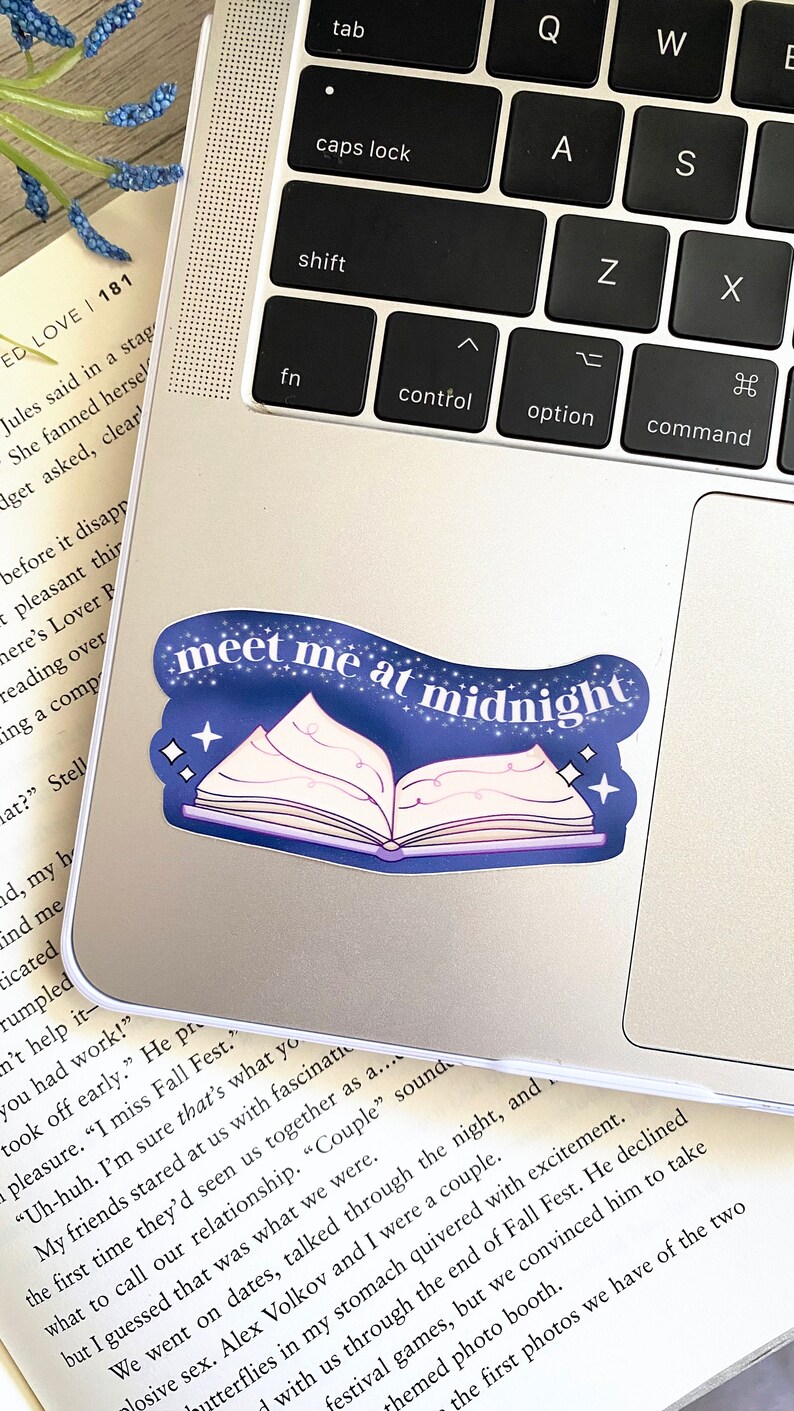 May include: A blue and white sticker with a book design and the text "meet me at midnight". The sticker is on a silver laptop.