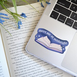May include: A blue and purple sticker with a book and stars on a laptop. The sticker says "Meet me at midnight".